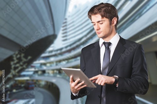 Thoughtful Businessman in a Suit Using digital tablet while Standing in Office
