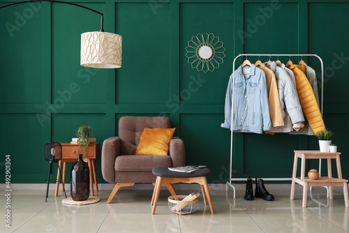 Interior of stylish room with modern furniture and hanger with jackets near green wall