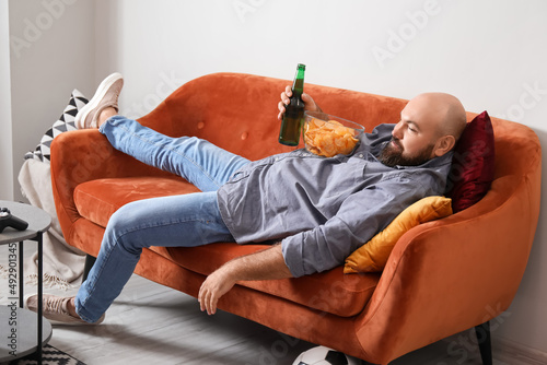 Funny lazy man drinking beer and eating chips while watching TV at home