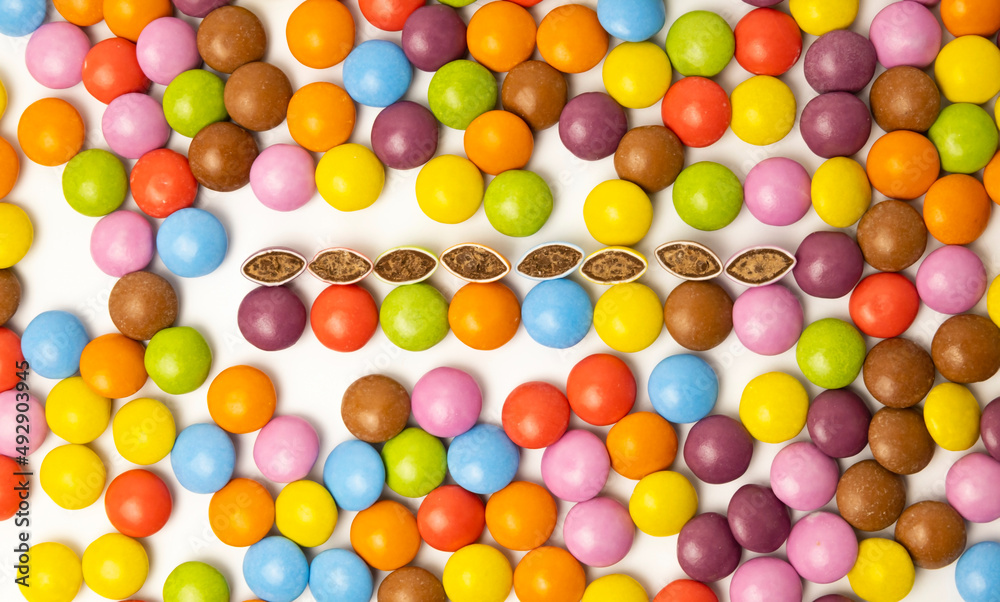 Obraz premium View from above. Chocolate candies of different colors laid out on a white background. The candies are cut in half. Harmful baby food