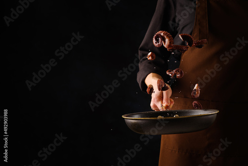 Chef roasts octopus pieces in frying pan. Concept of cooking seafood kitchen.On black background with empty space for inscription. recipe book.Asian cuisine
