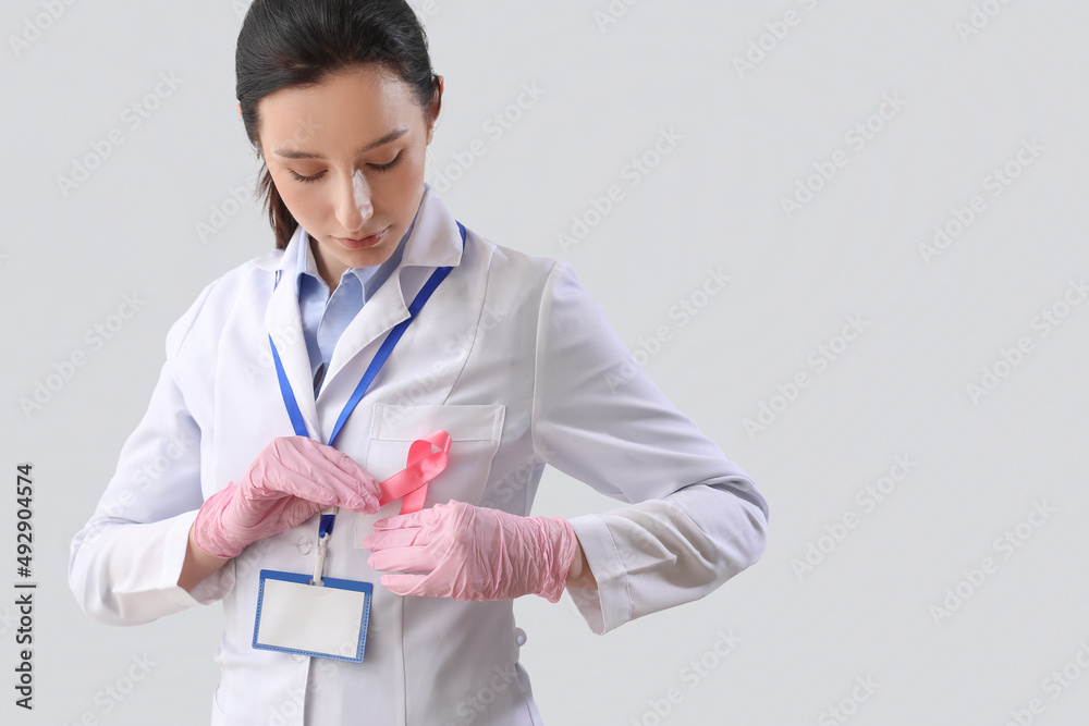 Female oncologist with pink ribbon on light background. Breast cancer awareness concept Female oncologist with pink ribbon on light background. Breast cancer awareness concept