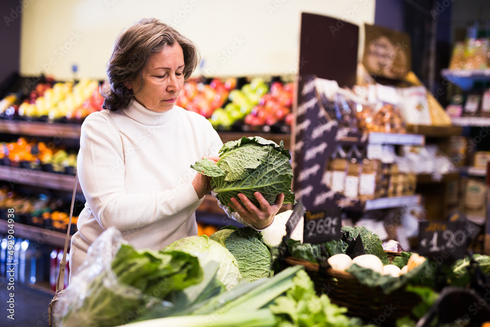 Mature woman choice ripe cabbage on grocery store shelves