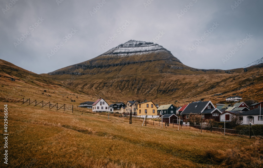 Colorful houses of Funningur village with a small river and outstanding mountains on background. Faroe Islands, Denmark. November 2021