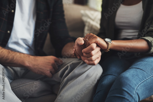 Hand in hand through it all. Shot of an unrecognizable couple holding hands while sitting on a sofa at home.