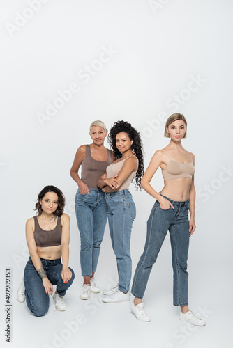 Young women posing near interracial friends on grey background.