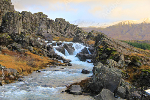 A beautiful mountain creek rushes with water in Iceland in a picturesque setting that is illuminated by beautiful colorful light with snow in the distance