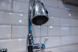 Low angle, selective macro focus on a stainless steel kitchen sink faucet, with water pouring in a thin steady stream