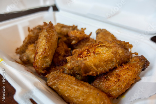 Close up, selective focus on an order of crispy chicken wings in a white styrofoam to-go container on a kitchen table