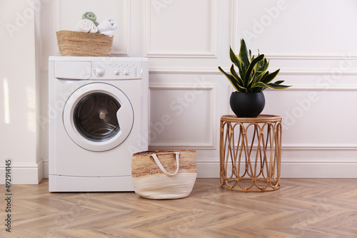 Laundry room interior with modern washing machine and beautiful houseplant near white wall © New Africa
