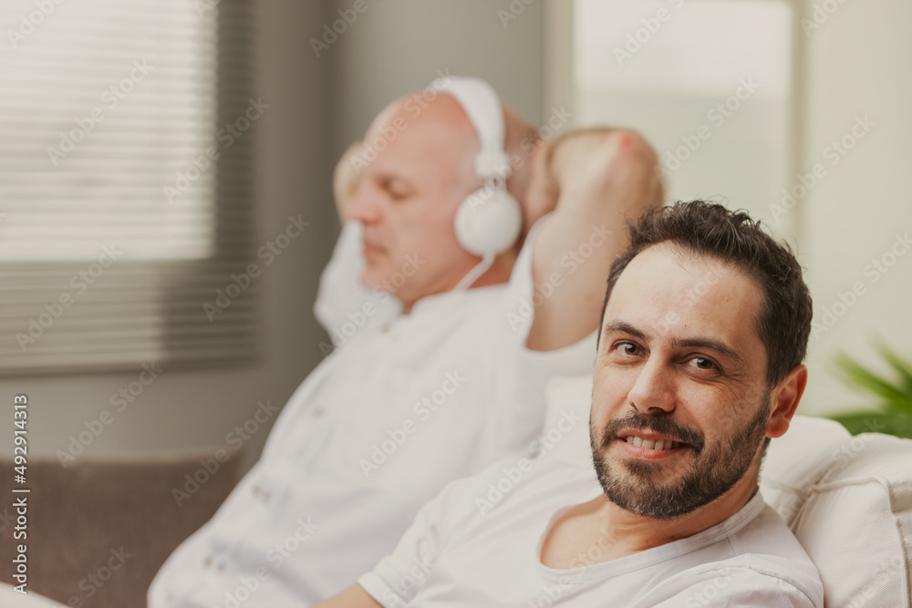 Fototapeta premium Man sitting smiling at the canera as his father listens to music