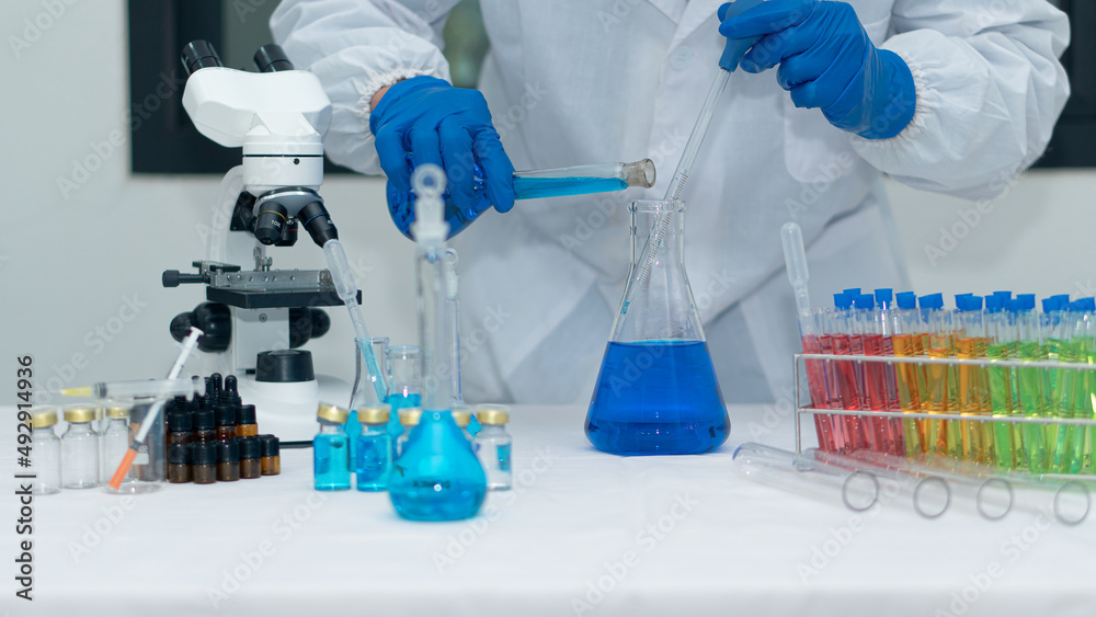 Fototapeta premium Scientist's hand tool holding a bottle with laboratory glassware in the background of a chemistry lab. Research and development concepts in science laboratories Medicine and Biotechnology