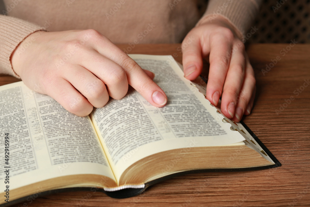 Woman reading Bible at wooden table, closeup Woman reading Bible at wooden table, closeup