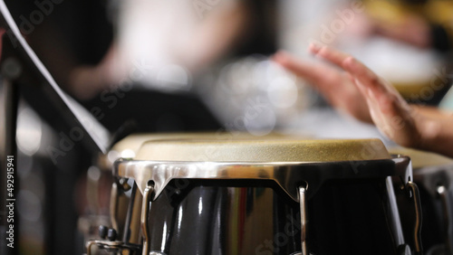 A close up of hands moving or in motion playing the congas or bongo style drums in a percussion section of a band or orchestra. Drum skin in focus. photo