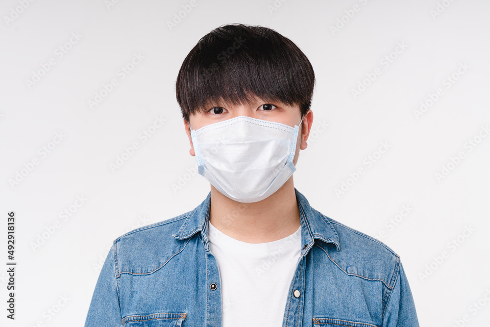 Young asian korean boy man student freelancer in denim shirt and protective face mask against Coronavirus Covid19 looking at the camera isolated on white background. Pandemic concept