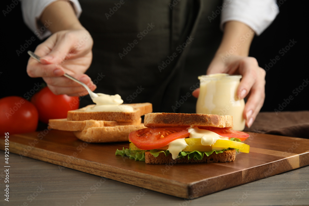Woman making sandwich with mayonnaise at wooden table, closeup