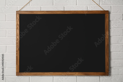 Clean black chalkboard hanging on white brick wall photo