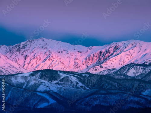 冬の北アルプス、夜明けの太陽の光りが雲に遮られ、山並みが直線状に照らし出されて赤く染まる、モルゲンロート