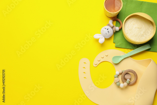 Healthy baby food in bowl and accessories on yellow background, flat lay. Space for text