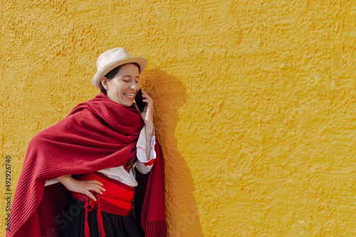 Latin peasant woman in typical costume talking on her mobile phone leaning against a rustic yellow wall