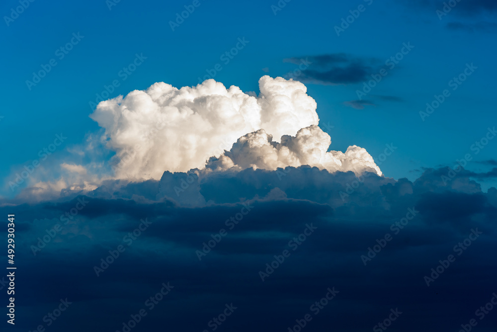 Naklejka premium A large cloud formation is brightly lit by the sun while dark storm clouds are below