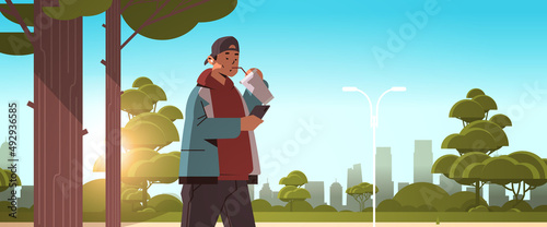 man drinking coffee with straw and using smartphone while walking in urban park social media communication digital addiction
