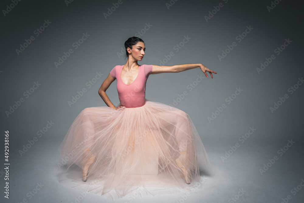 Naklejka premium young pretty, fragile, beautiful ballerina dancing in a long pale pink dress with tulle on a uniform background, hand movements, restrained tone. Ballet, dance, dancer. Place for inscription