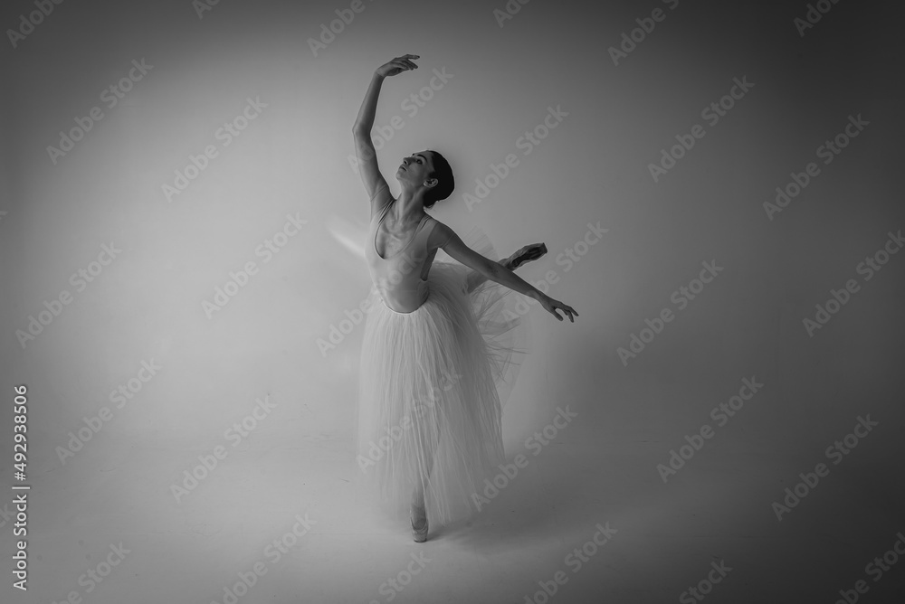 Naklejka premium classic black and white photo, young pretty, fragile, beautiful ballerina dancing in a long pale pink dress with tulle on a uniform background, restrained tone. Ballet, dancing, dancer selective focus