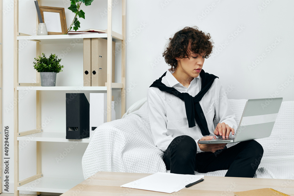 curly guy sitting on the couch at the table in front of a laptop Lifestyle technology curly guy sitting on the couch at the table in front of a laptop Lifestyle technology