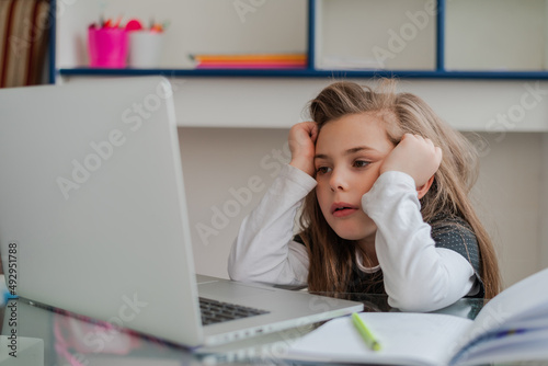 Tired kid student during the online education in the home. Bored child student while learning for school on a laptop. Unhappy girl student having problem with concentrate while attention online class.