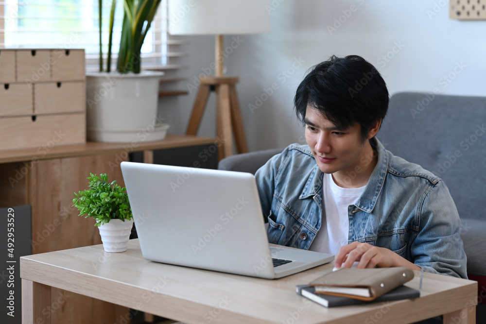 Asian male freelancer working online on computer laptop while sitting in living room. Asian male freelancer working online on computer laptop while sitting in living room.