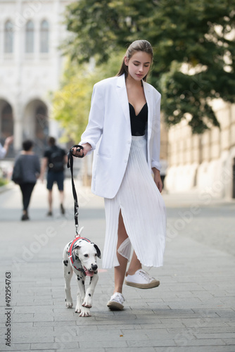 Woman walking with dog, street style. Fashion model in the city street. Fashion urban outfit. Casual everyday clothing style.