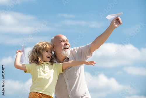 Φωτογραφία Young grandson and old grandfather with toy paper plane against summer sky background