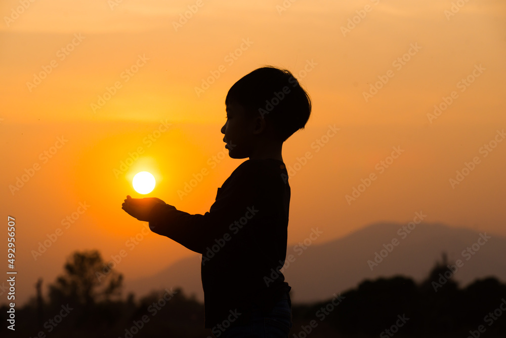 A boy playing with the sun at sunset. Silhouette picture with orange sunset sky. 