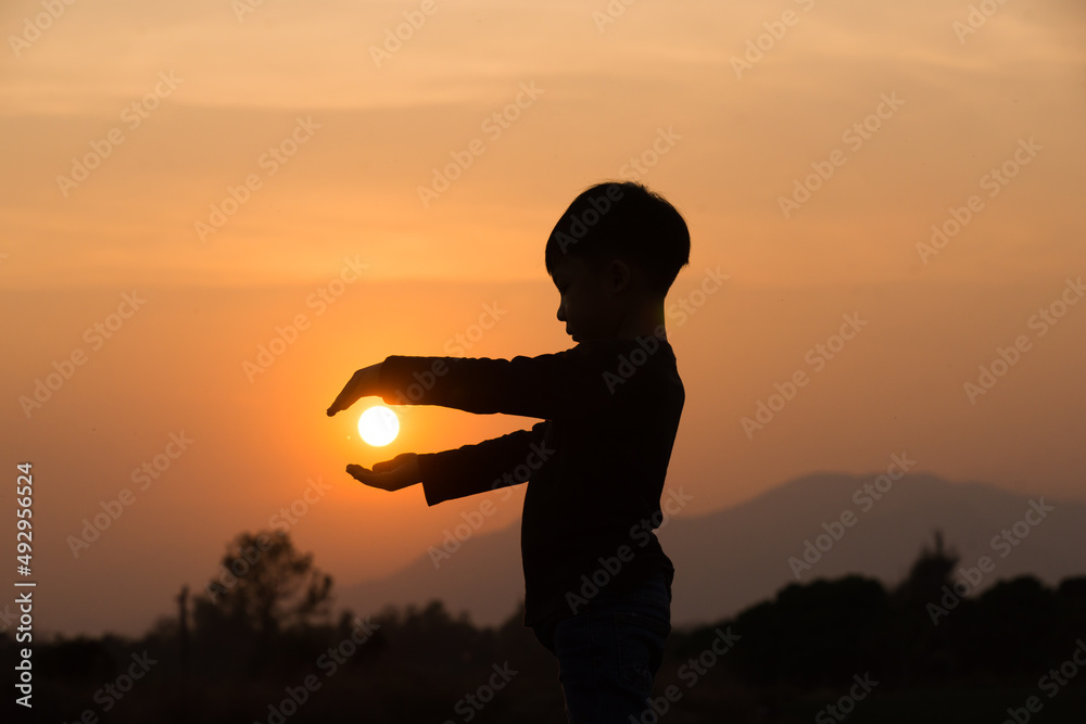 A boy playing with the sun at sunset. Silhouette picture with orange sunset sky. 