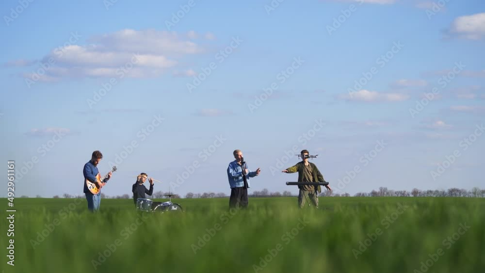 Music band of four guys perform song and instrumental music for drone footage. Gradual view transition from men at backdrop to green grass at foreground. Music band of four guys perform song and instrumental music for drone footage. Gradual view transition from men at backdrop to green grass at foreground.