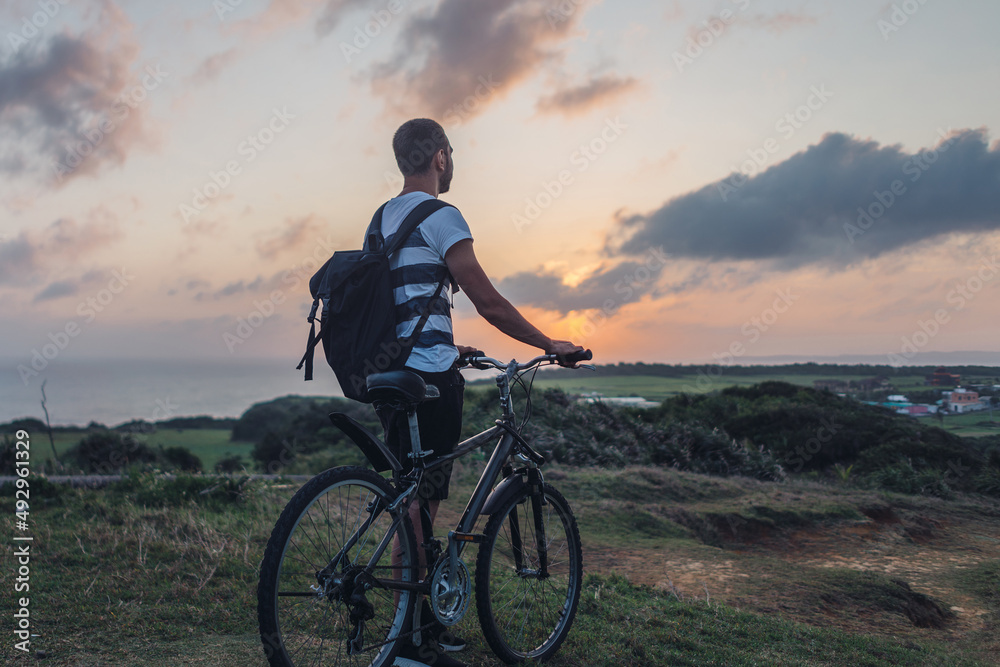 Fototapeta premium Young man stands with his bicycle in the evening and admires nature
