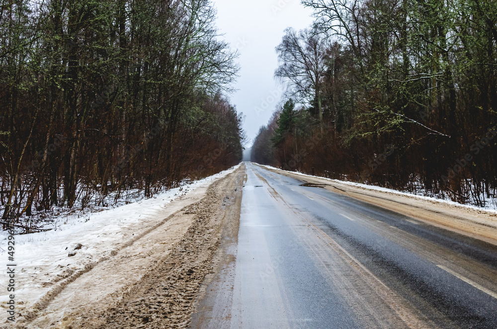 Dirty roadside in the winter period from reagents. A winter road goes into the distance through a mixed forest on a winter day