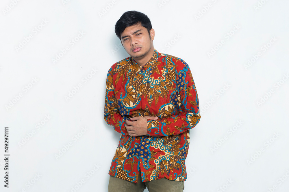 asian man wearing batik having a stomach ache isolated on white background asian man wearing batik having a stomach ache isolated on white background
