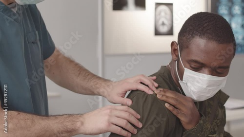 Medium closeup with slowmo of African American soldier with shoulder dislocation being examined by army doctor photo