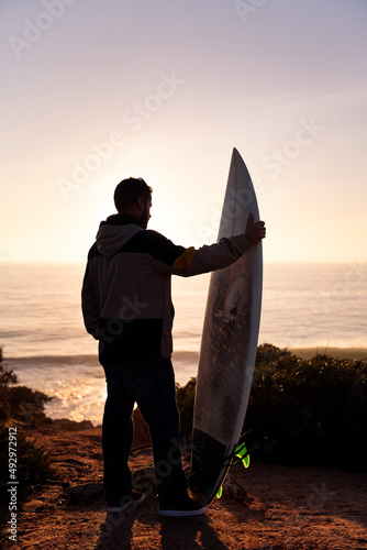 man looking at the sea at sunset with a surfboard