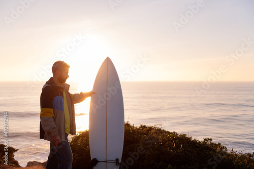 man holding his surfboard at sunset by the sea