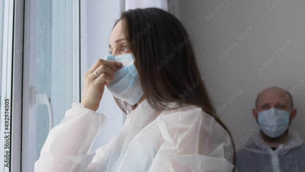 Tired health worker in the rest room dressed in masks, a female nurse adjusts her mask and looks out the window, a male doctor sits and rests after a serious operation with a fatal outcome. Tired health worker in the rest room dressed in masks, a female nurse adjusts her mask and looks out the window, a male doctor sits and rests after a serious operation with a fatal outcome.