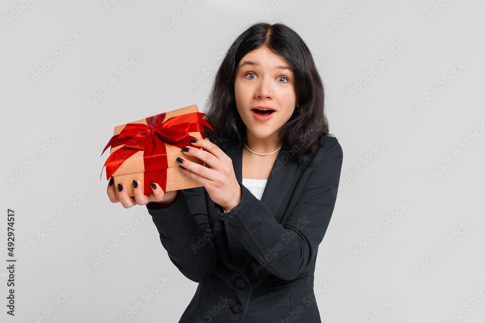 Cute brunette teenager girl in black blazer celebrating birthday, wonder whats inside b-day gift, opening box and and looking impressed with disbelief, grey background. Young emotional woman Cute brunette teenager girl in black blazer celebrating birthday, wonder whats inside b-day gift, opening box and and looking impressed with disbelief, grey background. Young emotional woman