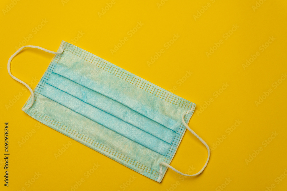 Close-up image of a blue face mask on a yellow background leaving copy space. Sanitary hygiene concept in times of viruses and diseases. Close-up image of a blue face mask on a yellow background leaving copy space. Sanitary hygiene concept in times of viruses and diseases.