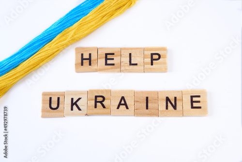 Top view phrase help ukraine is laid out of wooden squares isolated on white background. with flag of ukraine with blue and yellow ribbon. Concept of peace, war in Ukraine