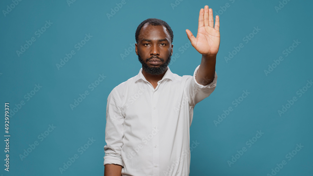 African american model raising palm to advertise stop sign in studio, expressing denial and refusal. Young adult showing rejection gesture with hand, denying access abnd feeling displeased.