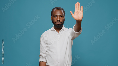 African american model raising palm to advertise stop sign in studio, expressing denial and refusal. Young adult showing rejection gesture with hand, denying access abnd feeling displeased. photo