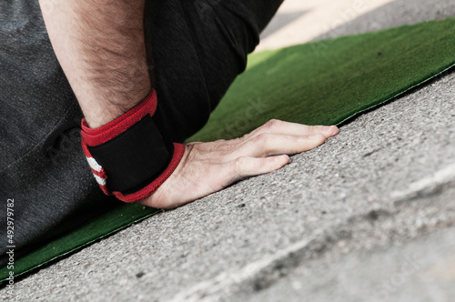 Close-up side view of a man s right hand with wrist band doing push ups on green mat