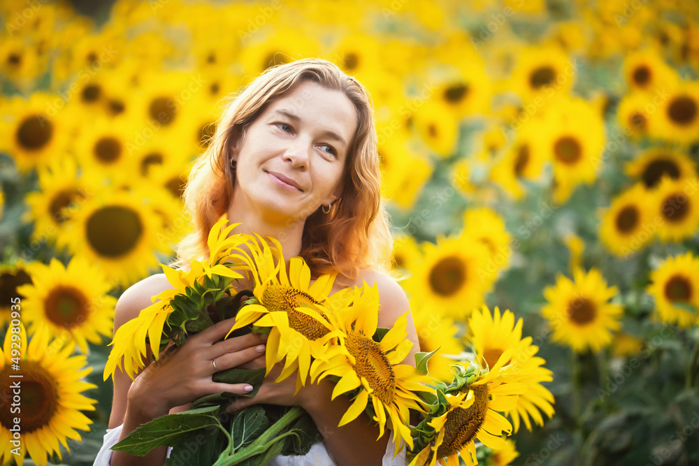 A beautiful woman with bare shoulders smiles in a sunflower field. The theme of cosmetology, skin care, vacation and relaxation in a calm atmosphere. A beautiful woman with bare shoulders smiles in a sunflower field. The theme of cosmetology, skin care, vacation and relaxation in a calm atmosphere.